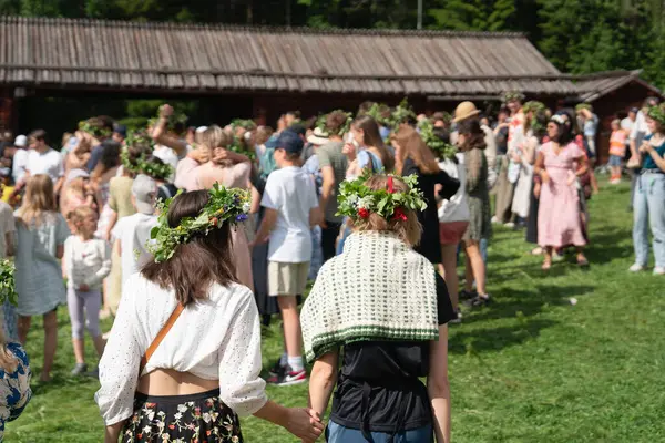 İsveç 'in Umea şehrinde yaz dönümü kutlamaları sırasında çiçek tacını takan iki kadın el ele tutuşup kameradan uzaklaşıyor. UMEA, GAMLIA, İSVEÇ 23 HAZİRAN 2023