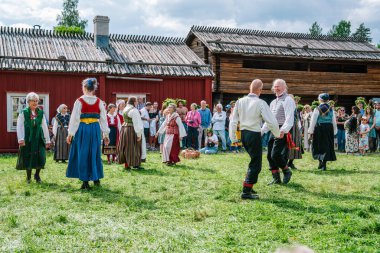 Geleneksel kıyafetler giyen yerliler dans ediyor ve diğer insanlar onları izlerken İsveç 'in Umea kentindeki Gammlia açık hava müzesinde yaz dönümünü kutluyorlar. UMEA, GAMLIA, İSVEÇ 23 HAZİRAN 2023