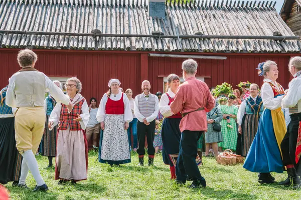 Geleneksel kıyafetler giyen yerliler, Gammlia, Umea, İsveç 'te kırmızı duvarlı ve gri çatılı ahşap bir evin önünde dans edip yaz dönümünü kutluyorlar. UMEA, GAMLIA, İSVEÇ 23 HAZİRAN 2023