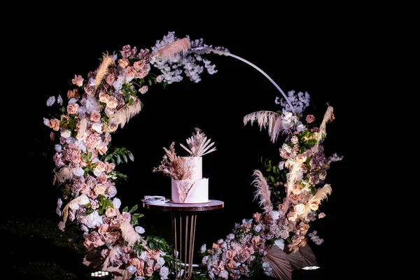 arch of flowers and cake at the wedding ceremony. Outdoor decoration. Romantic rustic style. The lamps are on in the evening.