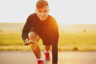 Koşucu, güzel ve büyük bir gülümsemeyle sokakta başlangıç pozisyonunda duruyor. Yüksek kalite fotoğraf