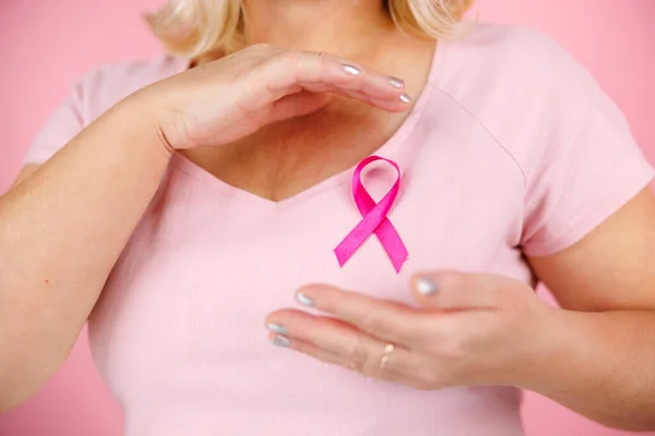 Closeup of pink badge ribbon on woman chest to support breast cancer cause. Healthcare, medicine and breast cancer awareness concept. High quality photo