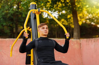 Young caucasian man wearing pale blue tank top and black pants and mask doing exercises in a calisthenics park. High quality photo