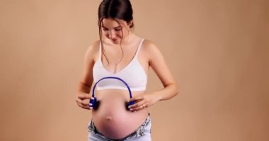 Hamile bir kadının göbeğinde müzik çalan büyük kulaklıklar. Doğmamış bebek anne karnındayken klasik müzik dinliyor. Erken dönem sanat ve yaratıcılık gelişimi kavramı