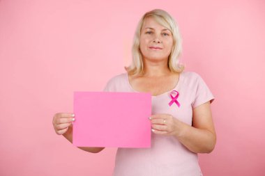 Elinde pembe bir kağıt tutan ve göğsünde pembe bir kanser kurdelesi olan kadın. Kanserle mücadele kavramı. Yüksek kalite fotoğraf