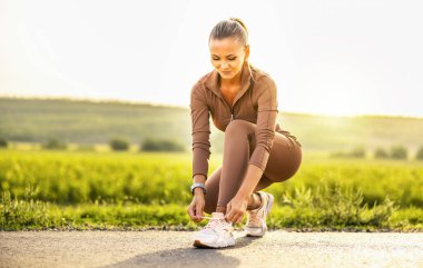 Genç bir sporcu. Ayakkabılarına ayakkabı bağlayan güzel bir sporcu kız. Güzel bir sporcu kız beyaz spor ayakkabılarıyla ayakkabı bağlıyor. Sağlıklı yaşam tarzı kavramı. Yüksek kalite fotoğraf