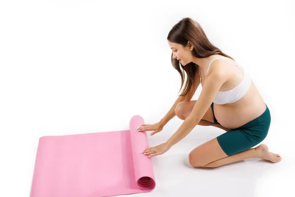 漂亮而快乐的孕妇正准备在白色背景的粉色瑜伽垫上进行体育锻炼 高质量的照片 — 图库照片