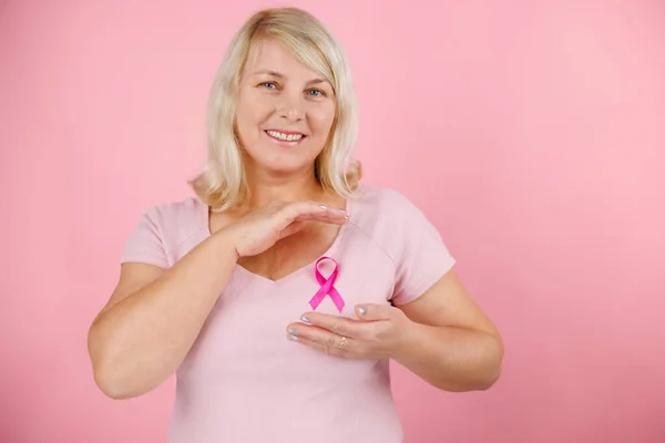 Woman holding pink cancer ribbon pointing thumb up to the side smiling happy with open mouth. High quality photo