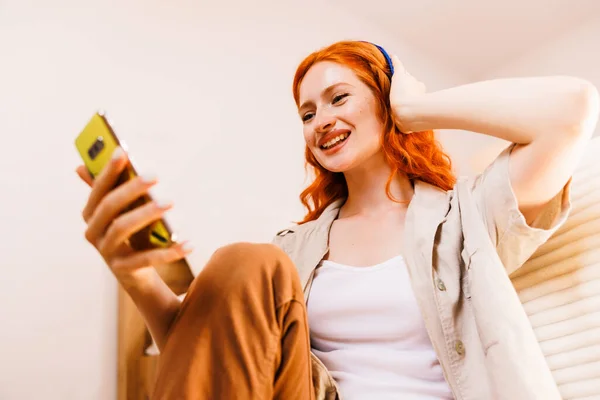 Młoda Szczęśliwa Kobieta Pomarańczowymi Włosami Pomocą Inteligentnego Telefonu Komórkowego Słuchawką — Zdjęcie stockowe
