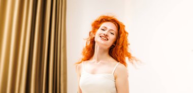 Dalgalı turuncu saçlı bir kadının portresi sabah ışıklarıyla odaya bakıyor. Hayat tarzı muhteşem bayan gülümserken hafif bir ışıkla mutlu oluyor. Yüksek kalite fotoğraf