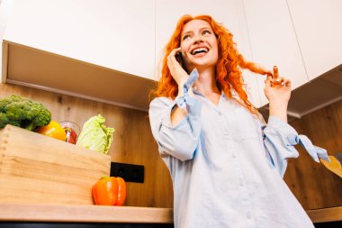 Mutlu aşçı kız mutfakta telefonla konuşuyor, akşam yemeği için taze sebzelerden salata pişiriyor, cep telefonuyla sağlıklı yiyeceklerle konuşuyor, gülümsüyor, gülüyor. Yüksek kalite fotoğraf