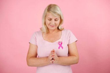 Pembe arka planda dua eden olgun bir kadın. Pembe bir tişört giyiyor ve pembe bir kanser kurdelesi var. Bu da kanserle mücadele anlamına geliyor. Yüksek kalite fotoğraf