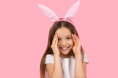 Gülümseyen ve kameraya bakan çok hoş bir kız. Paskalya konsepti olan tavşan kulağı takan avuçlarla yüzünü kapatmaya çalışıyor. Yüksek kalite fotoğraf