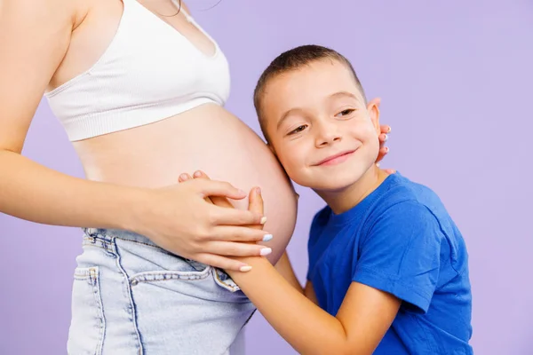 Niño Pequeño Abraza Una Madre Embarazada Sobre Fondo Púrpura Foto — Foto de Stock