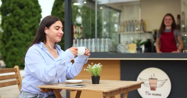 ヘッドフォンで音楽を聴きながら通りに座ってコーヒーを飲む女性の思考 高品質4K映像 — ストック動画