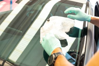 Cam değiştirildikten sonra arabanın ön camını silmek için elinde bez tutan yeşil eldivenli bir adamın elleri. Yüksek kalite fotoğraf