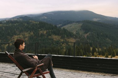 Genç adam bir fincan çay servisi yapıyor ve nefes kesici manzaralı bir dağ kalabalığında bir sandalyede meditasyon yapıyor. Yüksek kalite fotoğraf