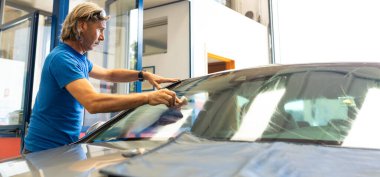 Araba yıkamada ön camı süngerle yıkayan mavi tişörtlü bir işçi.