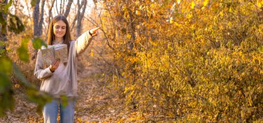 Genç bayan yürüyüşçü, sonbahar ormanı haritasını kullanarak güzel renkli doğa manzarasını gösteren bir işaret ile harika bir ruh hali içinde. Yüksek kalite fotoğraf