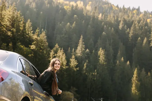 Freedom, travel and a happy woman looking back through the car window. Relaxation and happiness on the road of rural adventure. Travel, outdoor vacation in the mountains. High quality photo