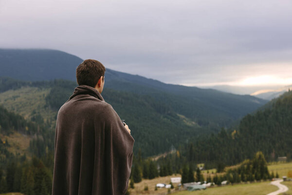 A young entrepreneur relaxes and meditates with a cup of tea in hand, watching a sunset on a mountain in the Carpathians. High quality photo