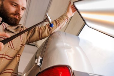 Adam arabadaki göçüğü onarmak için çekiç kullanıyor. Otomotiv aydınlatma ve jestlerle. Yüksek kalite fotoğraf