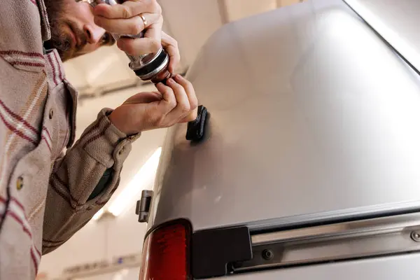 Aracın kapısı ve tamponu yakınında el hareketleriyle gümüş arabayı tamir eden adam. Yüksek kalite fotoğraf