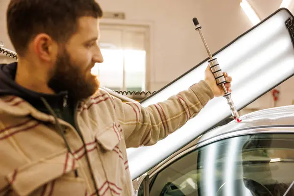 Garajda araba tamir eden sakallı bir adam dolu yüzünden hasar görmüş bir araba üzerinde çalışıyor. Yüksek kalite fotoğraf