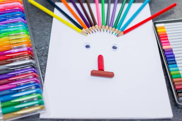 Colored pencils and an album for drawing. A funny face is made of colored pencils and chalk.