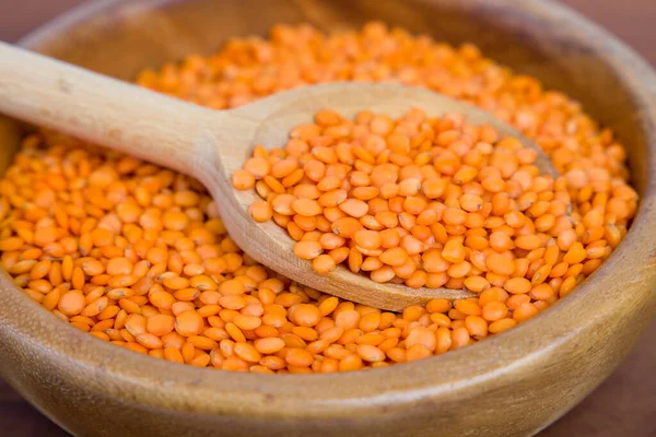 stock image red lentils in wooden spoon on a brown background