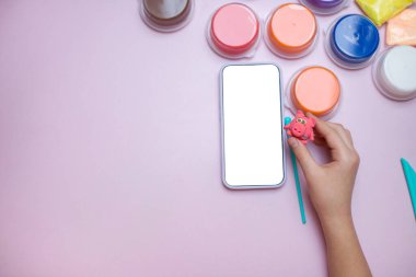 Boş ekranlı akıllı telefon, hava kuru kil ve pembe arka planda bir çocuğun elinde plastik figür..