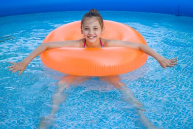 Yüzme havuzunda turuncu şişirilebilir yüzüklü şirin bir kızın portresi.