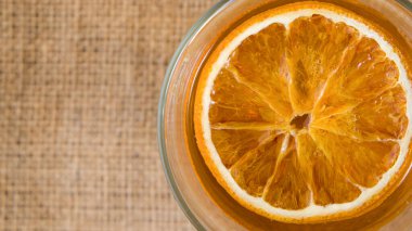 Cam fincanda portakal dilimleri ve çuval bezi arkaplanda çay.
