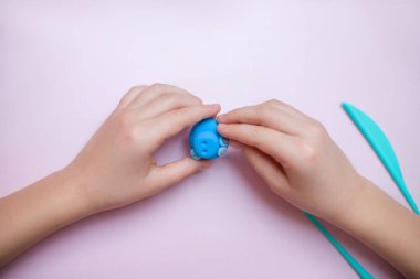 Çocukların elleri pembe arka planda mavi bir plastik tutuyorlar.