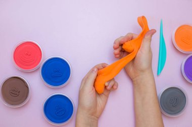 Çocuk elleri pembe arka planda turuncu bir balçık oyuncağı tutuyor..