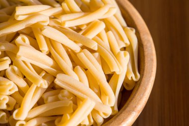 Tahta bir masanın üzerinde bir kase İtalyan makarnası, pişmemiş makarna. 