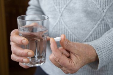 Elinde hap ve bir bardak su tutan yaşlı bir kadın..