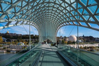 Tiflis, GEORGIA: 05 - 10 - 2022: Barış Köprüsü, Gürcistan 'ın eski Tiflis kentindeki Kura Nehri üzerindeki modern yay şeklinde yaya köprüsü.