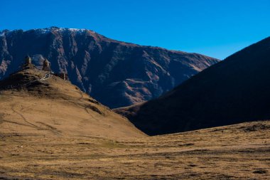 Kazbegi, Gürcistan: 10-11-2022: Antik Gergeti Trinity Kilisesi 'nin muhteşem manzarası ve muhteşem Kafkas dağları, güzel doğal dağ zirveleri ve çayırlar, Kazbegi, Gürcistan