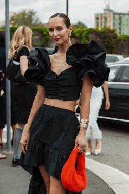 Misafir, Milano Moda Haftası Kadın Giyim / Yaz 2024 'te PRADA gösterisinin dışında görülen siyah küpe, siyah bluz ve etek, kırmızı tüylü çanta takıyor.