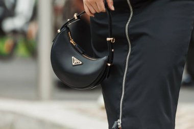 Moda detayları. Milan Moda Haftası Kadın giyim / Yaz 2024 'te PRADA gösterisinin dışında görülen siyah bir Prada önlü düz etek, siyah bir Prada çanta..