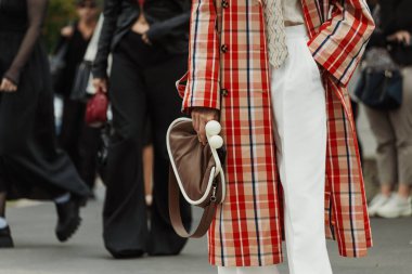 Milan Moda Haftası Kadın giyim / Yaz 2024 'te PRADA gösterisinin dışında kareli bir trençkot, beyaz pantolon, kravat ve kahverengi çanta giyen bir misafir görülüyor..