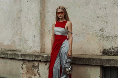 Bir konuk kırmızı gözlük takıyor, gri-kırmızı kıyafet, ayna çantası, Milan Moda Haftası Kadın Giyim / Yaz 2024 boyunca PRADA gösterisinin dışında görülüyor..