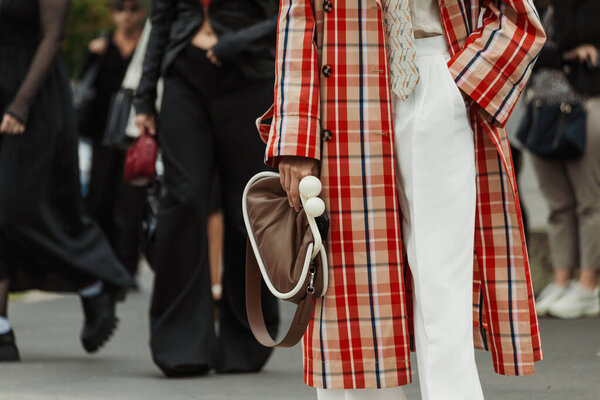 Гость в клетчатом плаще, белых брюках, галстуке и коричневой сумке, которого видели на выставке PRADA во время Миланской недели моды Женская одежда Весна / Лето 2024.