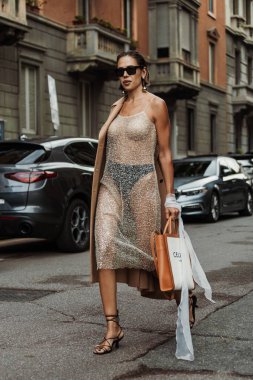 Bir konuk küpe, güneş gözlüğü, deve göğüslü bir ceket, transparan gümüş bir elbise giyer, Milan Moda Haftası Kadın giyim / Yaz 2024 'te MAX MARA gösterisinin dışında görünür..