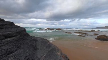Kayalık uçurum kıyıları ve dalgaların üzerine çöktüğü cennet manzarası. Sörfçü Praia do Castelejo 'daki kayalar Sagres yakınlarında. Portekiz 'in güneyindeki Algarve bölgesinin Batı Atlantik kıyıları.
