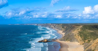 Kayalık uçurum kıyıları ve dalgaların üzerine çöktüğü cennet manzarası. Sörfçü Praia do Castelejo 'daki kayalar Sagres yakınlarında. Portekiz 'in güneyindeki Algarve bölgesinin Batı Atlantik kıyıları.