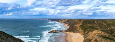 Kayalık uçurum kıyıları ve dalgaların üzerine çöktüğü cennet manzarası. Sörfçü Praia do Castelejo 'daki kayalar Sagres yakınlarında. Portekiz 'in güneyindeki Algarve bölgesinin Batı Atlantik kıyıları.
