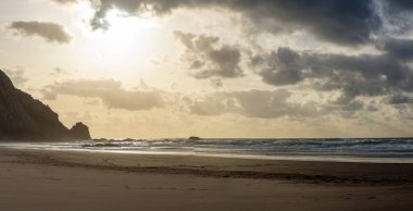 Kayalık uçurum kıyıları ve dalgaların üzerine çöktüğü cennet manzarası. Sörfçü Praia do Castelejo 'daki kayalar Sagres yakınlarında. Portekiz 'in güneyindeki Algarve bölgesinin Batı Atlantik kıyıları.