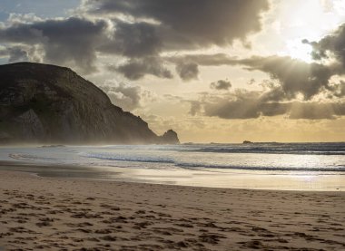 Kayalık uçurum kıyıları ve dalgaların üzerine çöktüğü cennet manzarası. Sörfçü Praia do Castelejo 'daki kayalar Sagres yakınlarında. Portekiz 'in güneyindeki Algarve bölgesinin Batı Atlantik kıyıları.